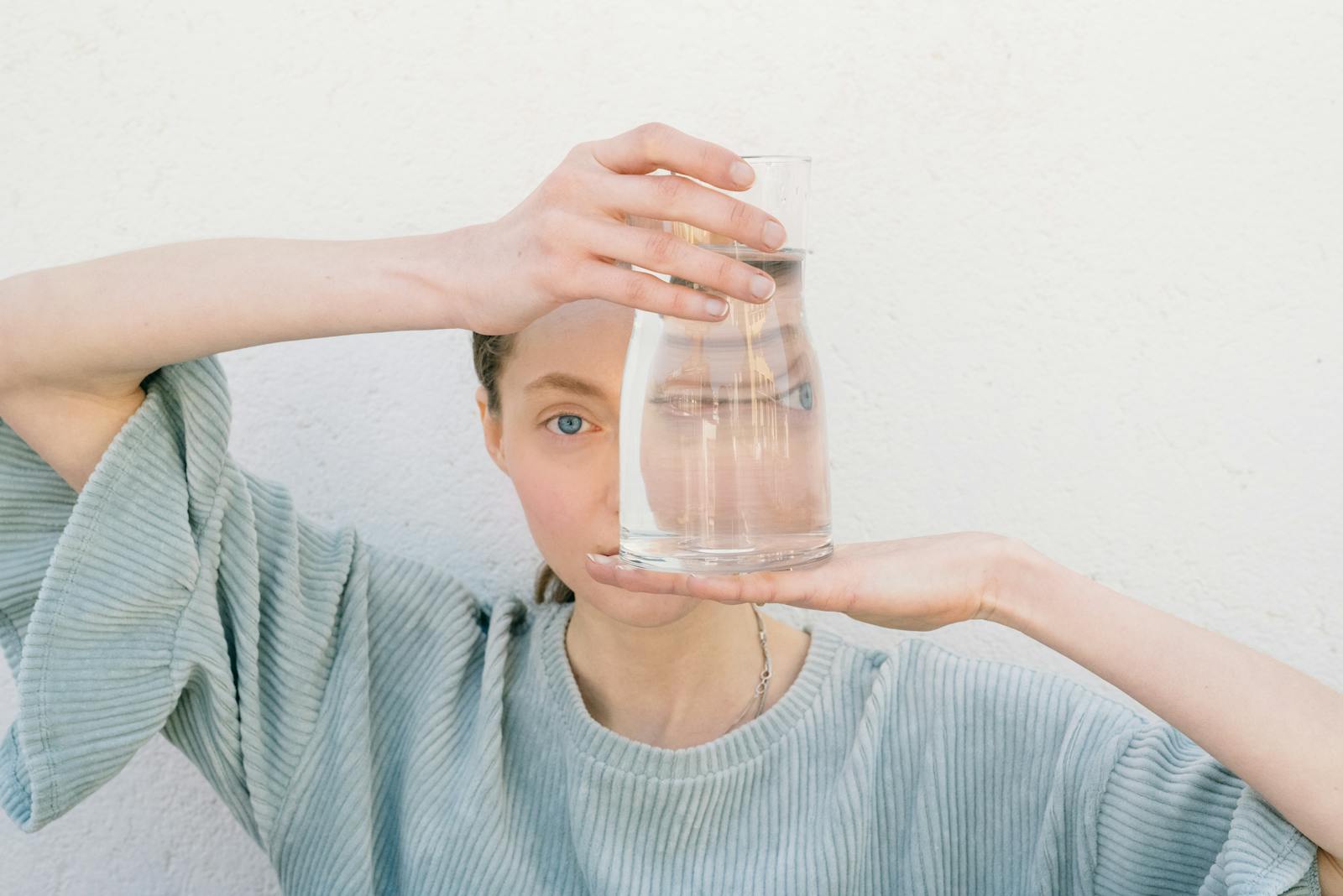 Woman holding a glass jug reflecting her face, creating a unique visual distortion.